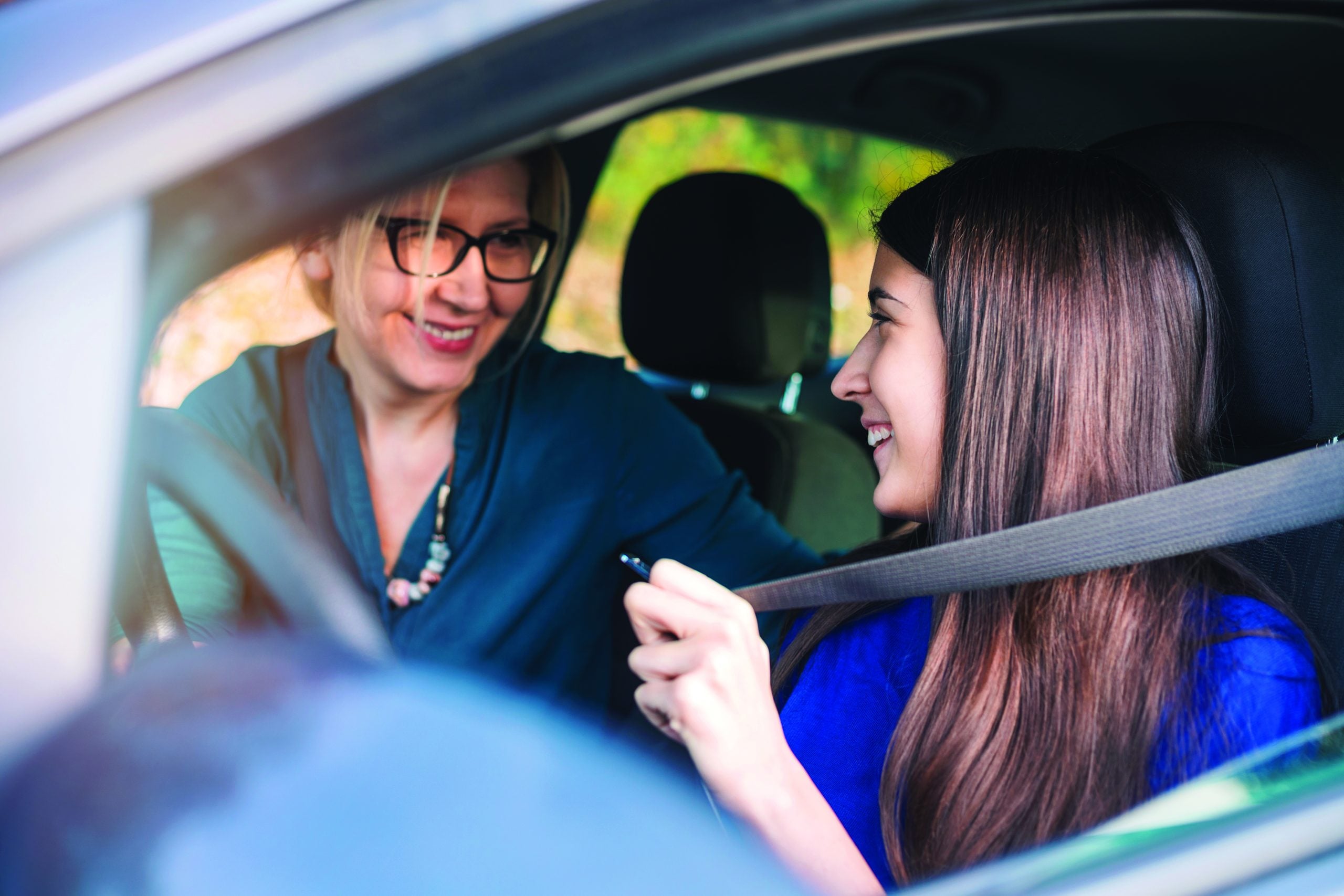 A teenage girl sitting behind the steering wheel of a car and listening to her mothers instructions as she drives.